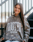 Camouflage Christian hoodie with bold ROOTED faith lettering and Colossians 3:3 scripture, styled on girl streetwear model.