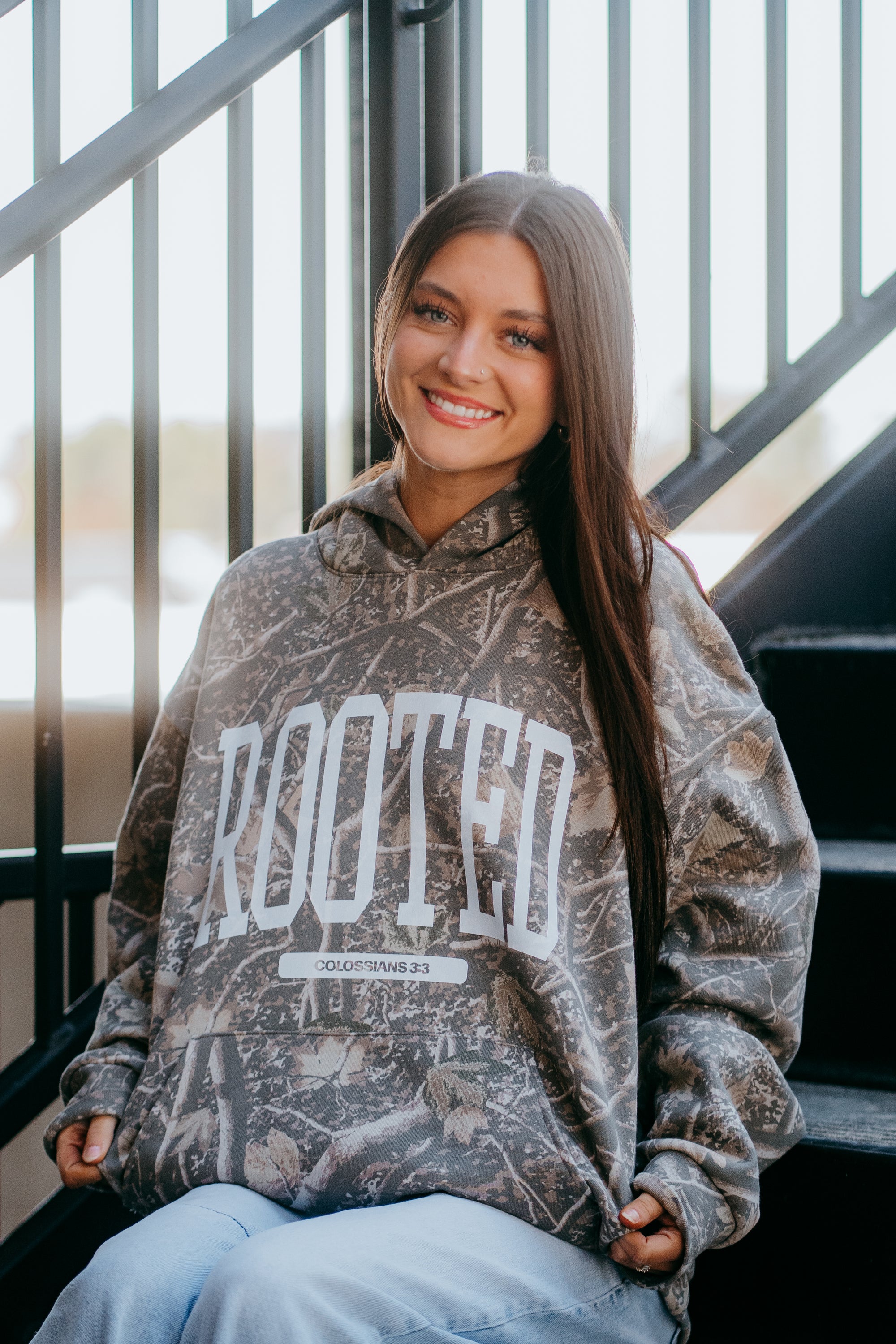Camouflage Christian hoodie with bold ROOTED faith lettering and Colossians 3:3 scripture, styled on girl streetwear model.