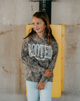 Girl wearing camouflage ROOTED hoodie, Christian streetwear design with bold faith-based lettering and Colossians 3:3 scripture detail.